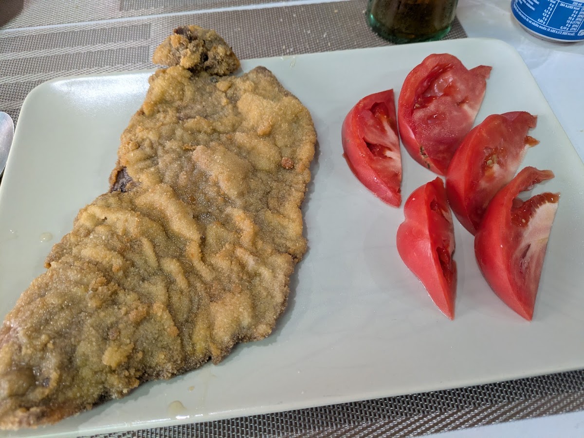 Filete de pescado empanado acompañado de rodajas de tomate fresco