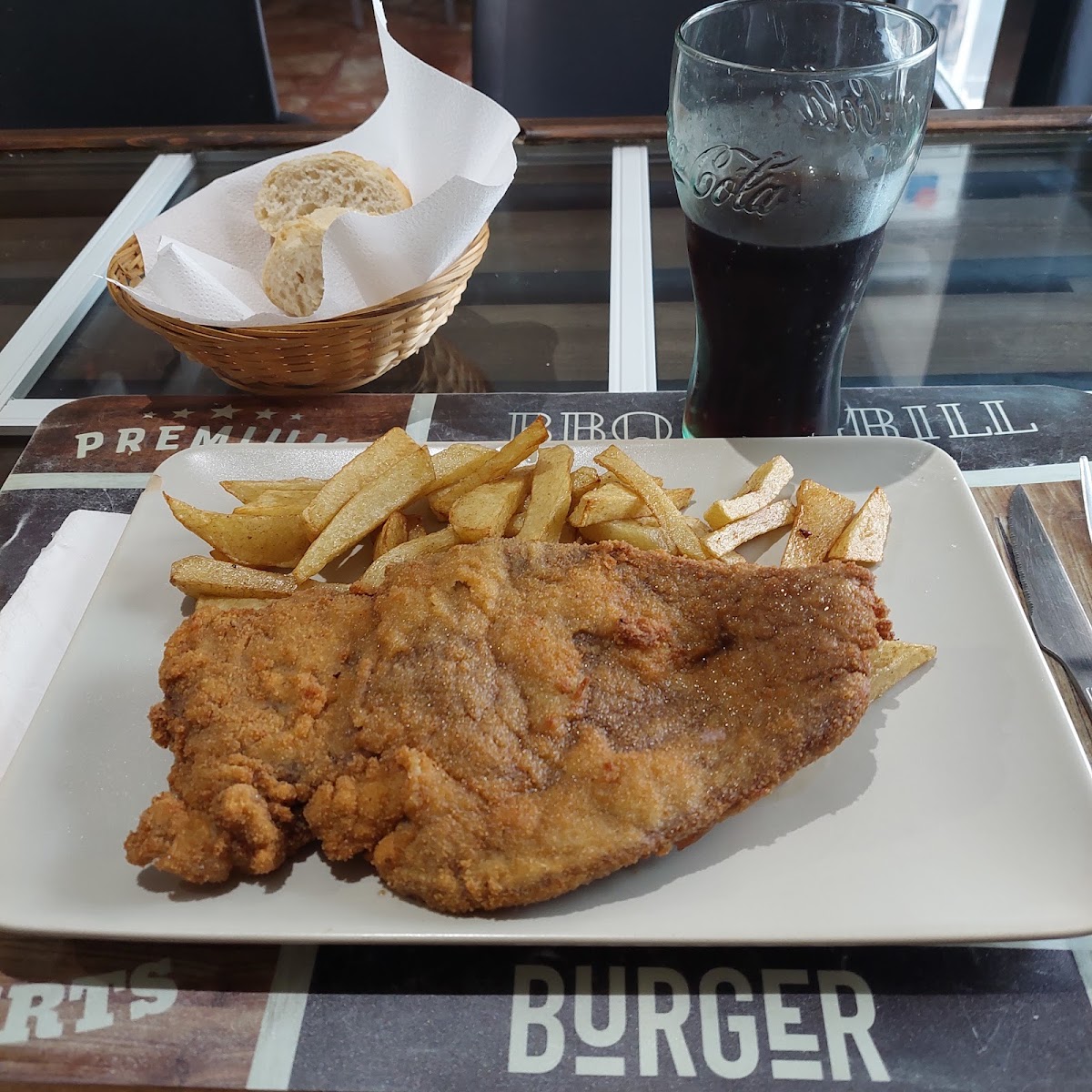 Plato de pescado empanado con patatas fritas y una bebida